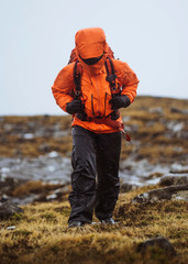 Woman in an orange windbreaker hiking under the rain at the Faroe Islands © rawpixel.com