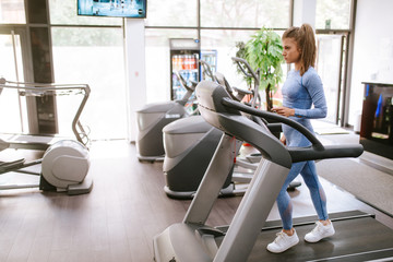 A beautiful young caucasian girl is running in the gym on a treadmill