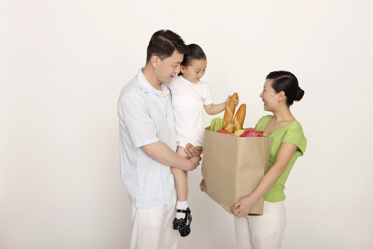 Woman holding a bag of groceries, man carrying girl