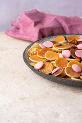 Small pancakes cereal in ceramic bowl on light beige background. Dalgona coffee and tiny pancakes cereal Served with pink and milk chocolate drops