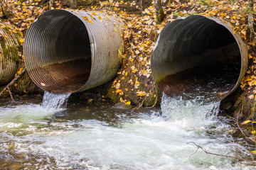 Old aging infrastructure. Three perched old and rusty culverts creating a barrier to fish in a stream on a forest road. - obrazy, fototapety, plakaty