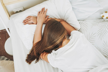 Young woman with long dark hair sleeping in bed with white linen at the bright bedroom