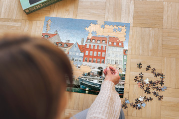 Woman assembling a jigsaw puzzle of Nyhavn, Copenhagen during coronavirus quarantine.