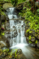 Fototapeta na wymiar Landscape. Small cascade waterfall. Nature background. Slow water flow. Stream with stones in tropical forest. Slow shutter speed.