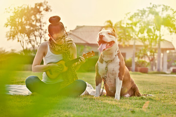 Women playing ukulele guitar  in the park on the grass with pitbull dog at sunset