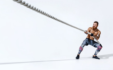 Strong man pulling rope. Photo of sporty man on white background. Strength and motivation. Side view. Full length