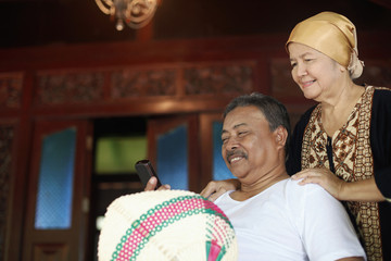 Senior man reading text message, senior woman standing behind him