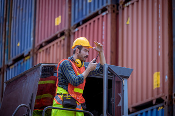 A dock worker under discussion about dock container shipping warehouse working, he wearing safety uniform hard hat ,earphone and hold radio communication.