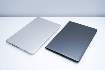 A dark grey laptop and a silver laptop are on the white desk