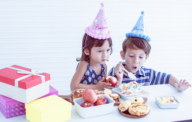 Caucasian little boy and girl surprising and being happy while celebrating birthday. There are foreground of presents, apple and bakery. Party and Education concept.