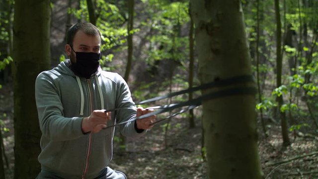 Young Bearded Man in Face Mask Exercising with Resistance Bands in Lush Forest