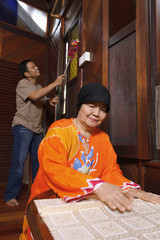 Senior woman folding table cloth while man is dusting the house