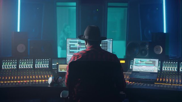 Producer, Audio Engineer Uses Control Desk for Recording New Album Track in Music Record Studio, in the Soundproof Room Musician, Artist, Performer Sings a Song from New Album. Back View 