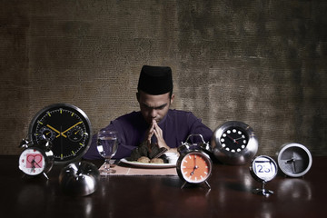 Man saying a prayer before starting his meal, alarm clocks on the table