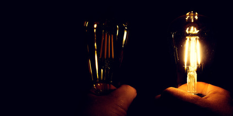 Ideas and innovation concept; Hands are holding retro type light bulbs on black background. One is in the dark. Other lamp is lightened. Enlightenment of the soul and creative inspiration