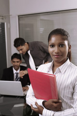 Businesswoman holding folder, businessmen discussing in the background