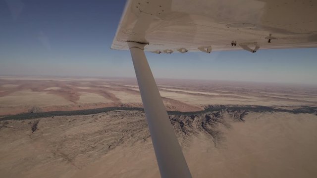 Aerial shot of plane flying over arid landscape against sky, scenic view of desert on sunny day - Sossusvlei, Namibia