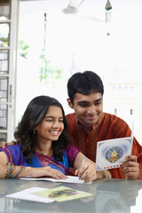 Teenage girl writing greeting card, young man reading