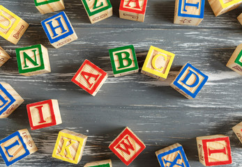 Multicolored wooden cubes with letters on gray background. Set for studying alphabet. Education, back to school concept. Top view, copy space	