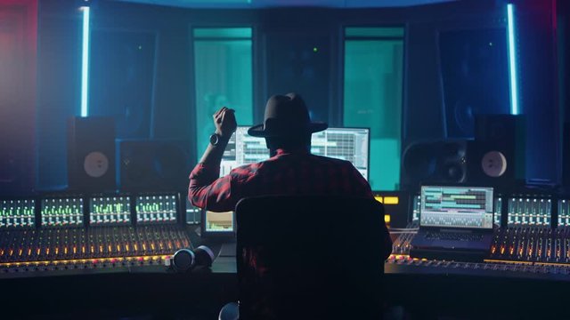 Producer, Audio Engineer Uses Control Desk for Recording New Album Track in Music Record Studio, in the Soundproof Room Musician, Artist, Performer Sings a Song from New Album. Back View 