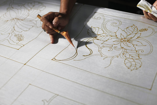 Man drawing batik patterns on fabric