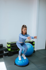 A beautiful young caucasian girl in blue sports equipment does squats in the gym