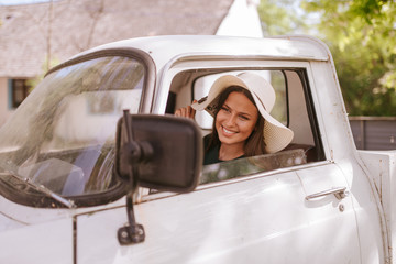 A beautiful young woman with a straw hat drives an old white truck. Life in a village