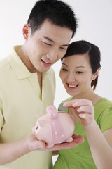 Pregnant woman putting coin into piggy bank, man holding the piggy bank