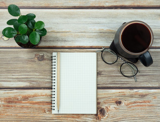 Top view desktop with supplies, in bright wooden background, blank notebook with pencil on top, vintage eyeglasses, during work from home.