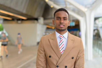 Happy young handsome African businessman smiling at the footbridge