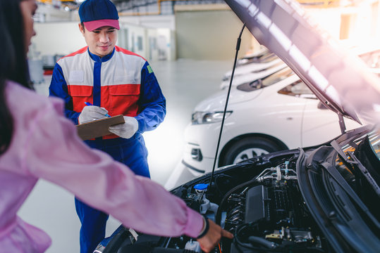 An Asian male car mechanic and a beautiful Asian customer is talking and agreeing to fix a girl's car in a car repair shop.