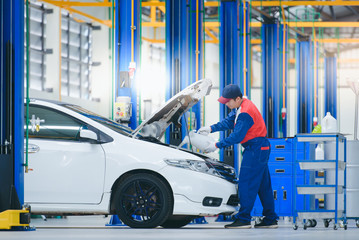 The car mechanic in the repair shop is filling the engine oil by pouring engine oil into the engine. For customers who use cars for repair services, a car mechanic works in the garage.