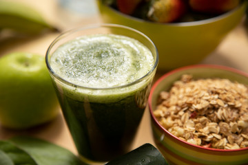 green smoothie in glass cup with granola with fruits in the background