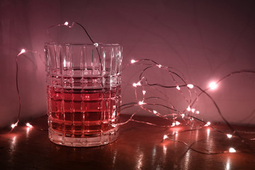 A whiskey glass with liquid in it, surrounded by magical Christmas fairy lights and a gradient glow