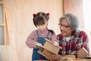 Senior male asian carpenter and grandchild making wooden bird house at home . Little asian girl...