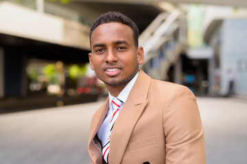 Obraz premium Happy young handsome African businessman smiling in the city outdoors