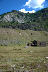 An old dilapidated building without a roof stands at the foot of a high hill.
