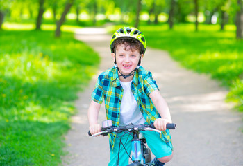 Naklejka premium A boy with a green bicycle helmet on his head rides his bicycle in the summer park. Summer rest