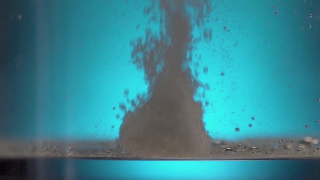 Close up stylized slow motion of effervescent tablet dropping to bottom of glass with fizzy bubbles.