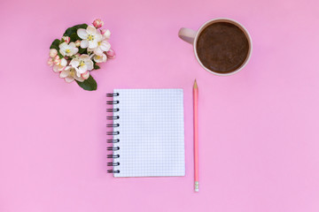 A notebook for notes lies on a pink background, next to  pen, coffee and flowers. Planning
personal time and works  