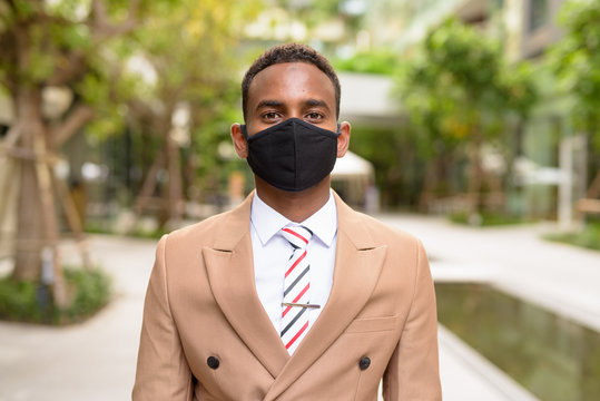 Young African businessman wearing mask for protection from corona virus outbreak in the city with nature