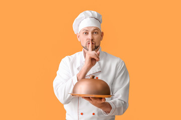 Portrait of male chef showing silence gesture on color background