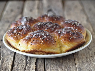 Homemade cake.Buns filled with jam, sprinkled with sesame seeds and icing sugar on a porcelain plate on an ancient wooden table.