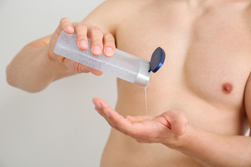 Handsome man with shower gel on light background