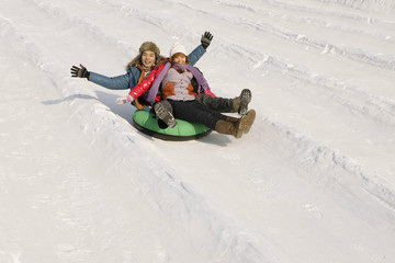 Fototapeta na wymiar Man and woman sliding down snowy hill on inner tube