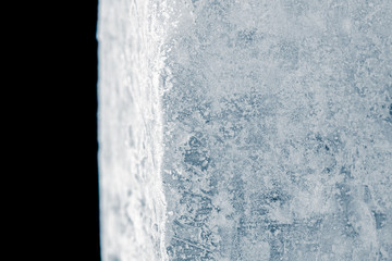 Fragment of frosty, textured, blue toned, natural ice block, on black background.