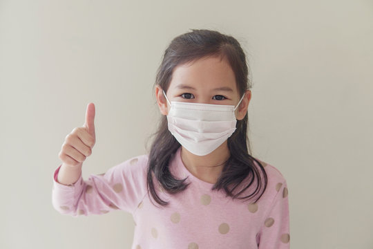 Mixed Asian Student  Girl Wearing Mask And Giving Thumb Up, School Reopening, Return Back To School After Covid-19 Coronavirus Pandemic Is Over, New Normal Concept