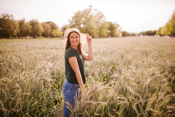 A beautiful attractive smiling caucasian woman with a straw hat in a field of grain