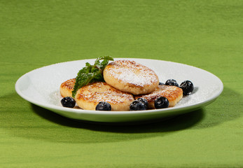 pancakes with blueberries, mint leaves and icing sugar on a plate, morning homemade breakfast for breakfast, a white dish on a green napkin, closeup of food