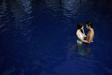 Couple standing in pool, looking at each other